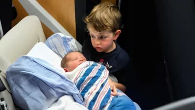 A little boy standing next to a newborn baby